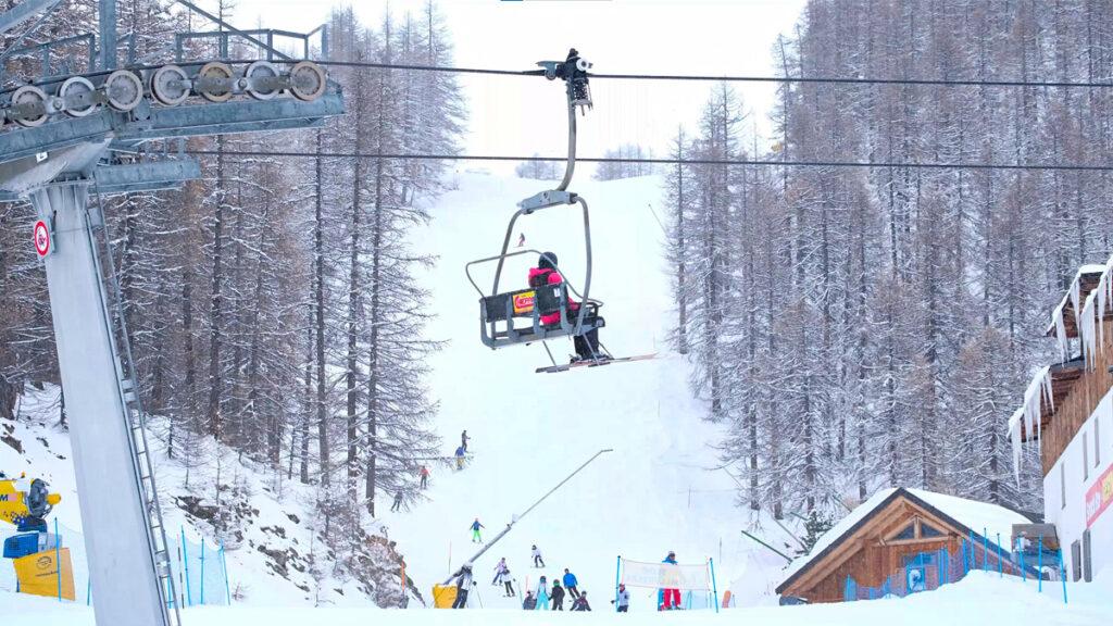 Skiers on a ski lift with a slope in the background and skiers beneath them.