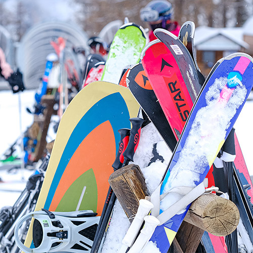 Snowboards and skis stacked on a stand outside.