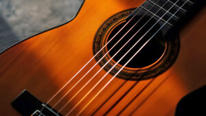 A close-up of a classical guitar, focusing on the soundhole and the strings. The guitar is a warm brown color, and the strings are taut.