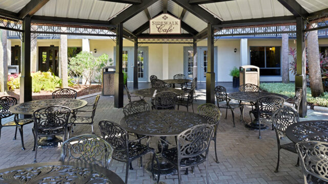 An outdoor cafe area with a covered gazebo and wrought iron tables and chairs. The cafe is called 