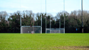 Green grass on a training field in focus, Two tall goal posts for Irish National sports camogie, hurling, rugby, gaelic football, soccer. warm sunny day, Nobody. Outdoor activity concept.