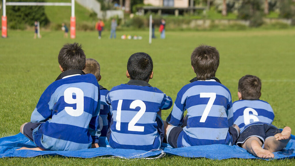 Rugby players sitting in a huddle with their backs to the camera.